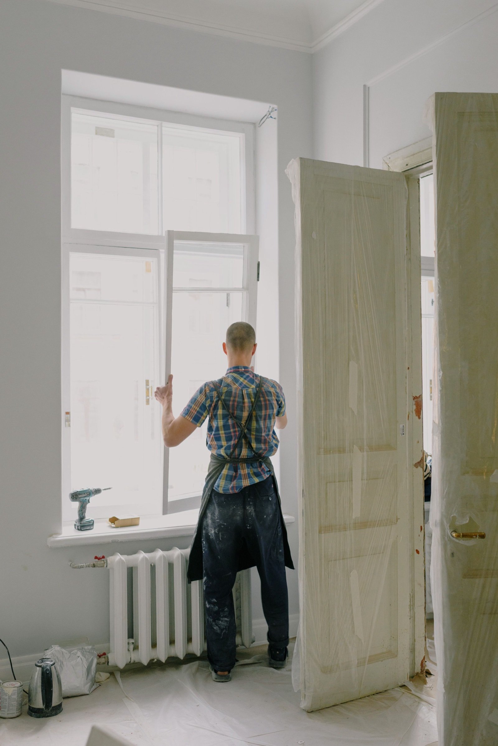 Tradesman in an apron fitting a new window frame in a bright room with tall panel doors